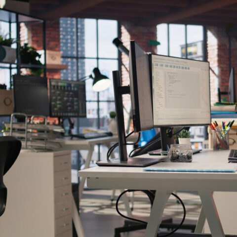 Modern office space with desks, monitors, and large windows overlooking cityscape